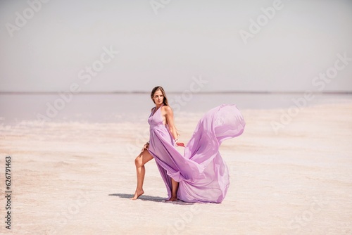 Woman pink salt lake. Against the backdrop of a pink salt lake, a woman in a long pink dress takes a leisurely stroll along the white, salty shore, capturing a wanderlust moment.