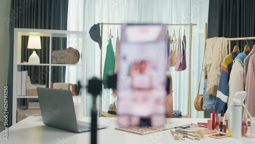 Young Asia lady beauty blogger wear crop top looking at phone camera live stream use digital tablet talk follower introduce her chanel ask audience like subscribe share her chanel at house studio.