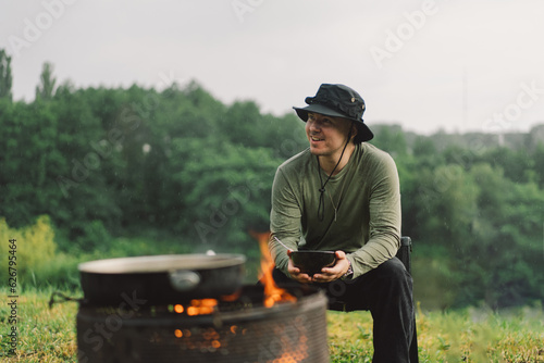 A man enjoy the food by the fire. Hiking camp with a bonfire in the forest. Tourist on recreation outside. Campsite lifestyle