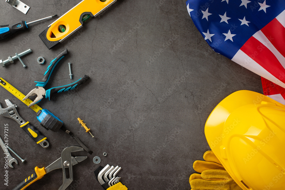 Commemorating construction workers' contributions on American Labor Day. Above photo of flag, helmet, gloves, and building tools on grunge textured grey concrete with copyspace ideal for ads or text