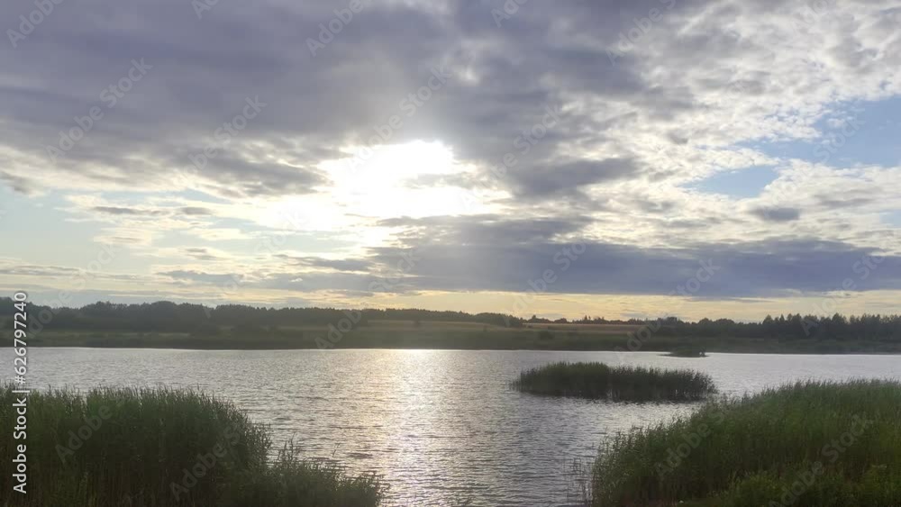 Beautiful evening lake with grassy island and shore view with cloudy sky at summer evening. West Russian natural landscape Beautiful evening lake with grassy island and shore view with cloudy sky at summer evening. West Russian natural landscape