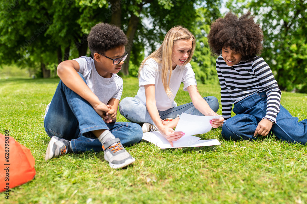 Blonde volunteer sitting on the grass and helping kids with tests Blonde volunteer sitting on the grass and helping kids with tests