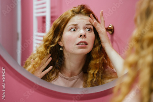 Worried woman examining face looking in mirror at home photo