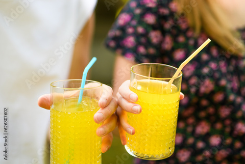 Trzymane w dłoniach szklanki ze słomką i sokiem pomarańczowym 