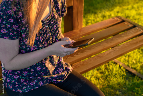 Kobieta siedzącą na ławce w parku korzystająca z telefonu komórkowego 