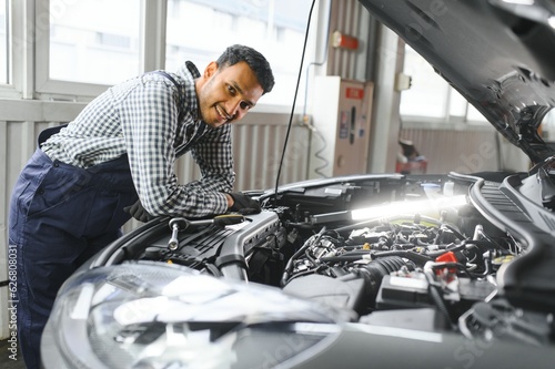 latin hispanic auto mechanic in uniform is examining a car while working in auto service