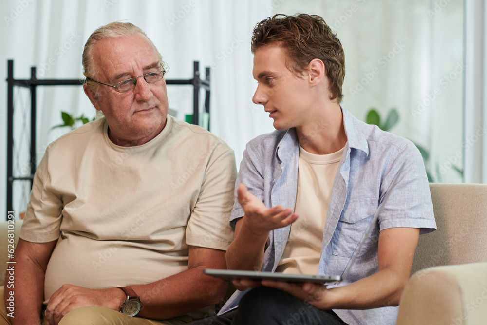 Obraz premium Positive young man explaining grandfather how to install apps on tablet computer