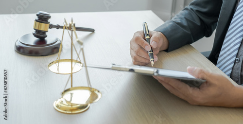 Lawyer hand holding pen and providing legal consult business dispute service at the office with justice scale and gavel hammer