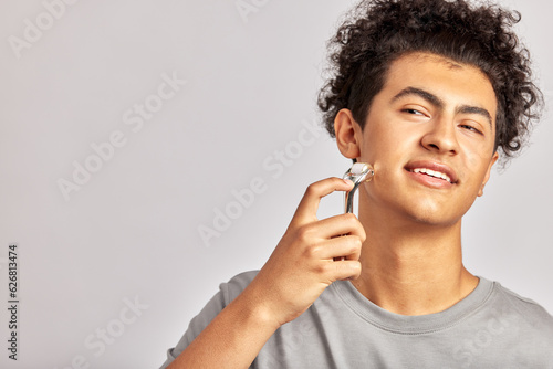 Young handsome smiling guy using de-puffing face roller to keep his skin soft and smooth. Swarthy man with black curly hair maintains his natural beauty with a skincare routine. Men's self-care.