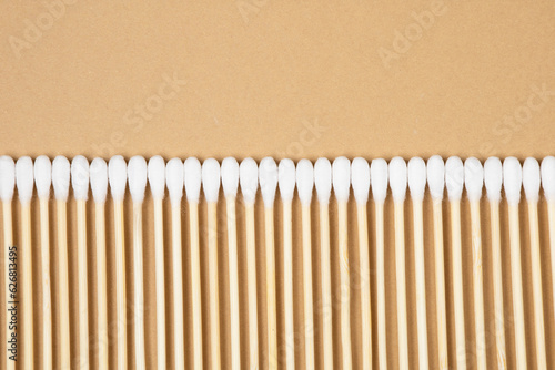 Many wooden cotton buds lie in a row on a beige background made of craft paper