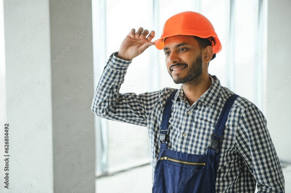 Indian construction site manager standing wearing helmet, thinking at construction site. Portrait of mixed race manual worker or architect. Indian construction site manager standing wearing helmet, thinking at construction site. Portrait of mixed race manual worker or architect.