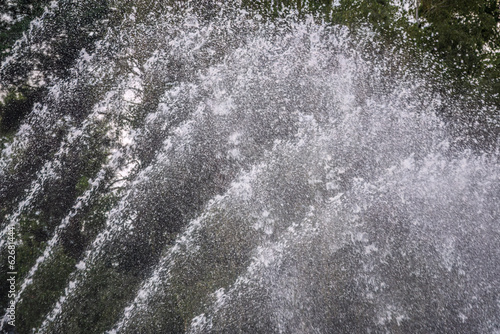 Splashes of water on dark background. Water sprays in sunny day close-up.