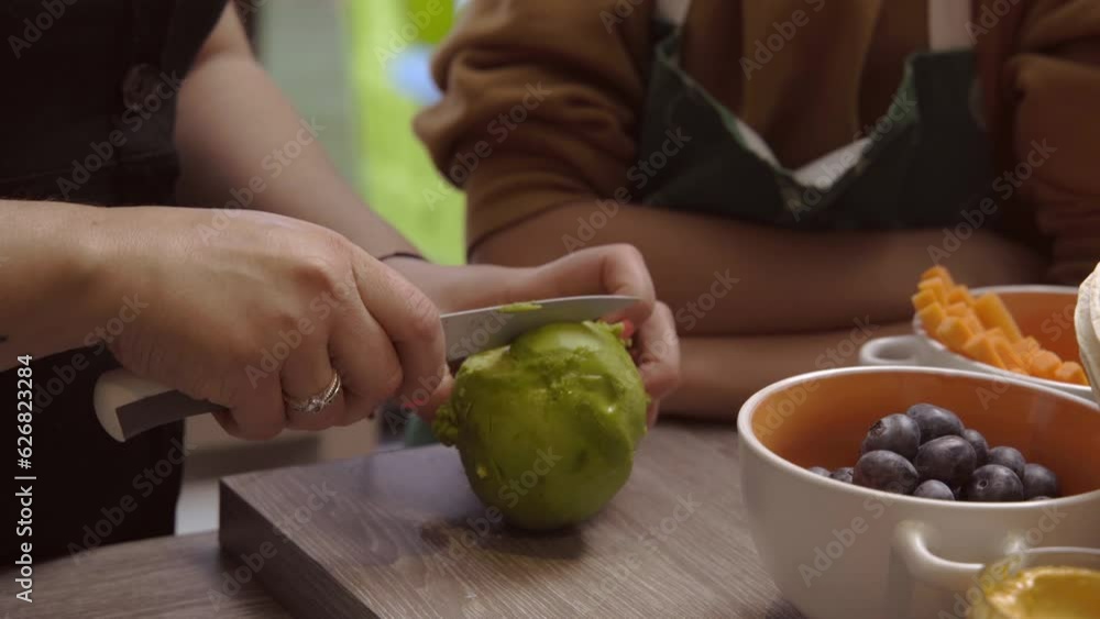 Close-up of a woman and her son slicing an avocado on a board - Videos of families cooking. Close-up of a woman and her son slicing an avocado on a board - Videos of families cooking.