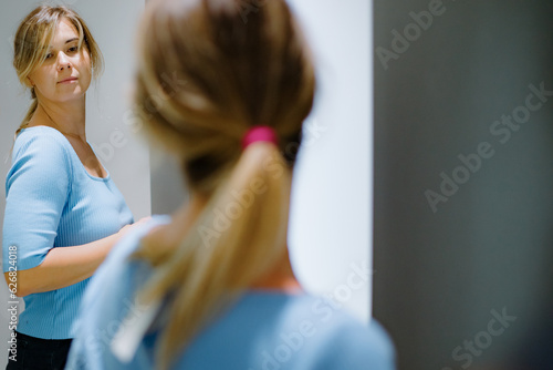 Fotografía Delightful lady standing in dressing room, trying on blue t-shirt and checking new outfit in mirror at clothes store