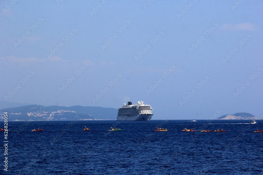 
Bright blue water and white cruise liner in the Adriatic Sea, many colorful canoes with people in the foreground, mountains in the background, Dubrovnik, Croatia
