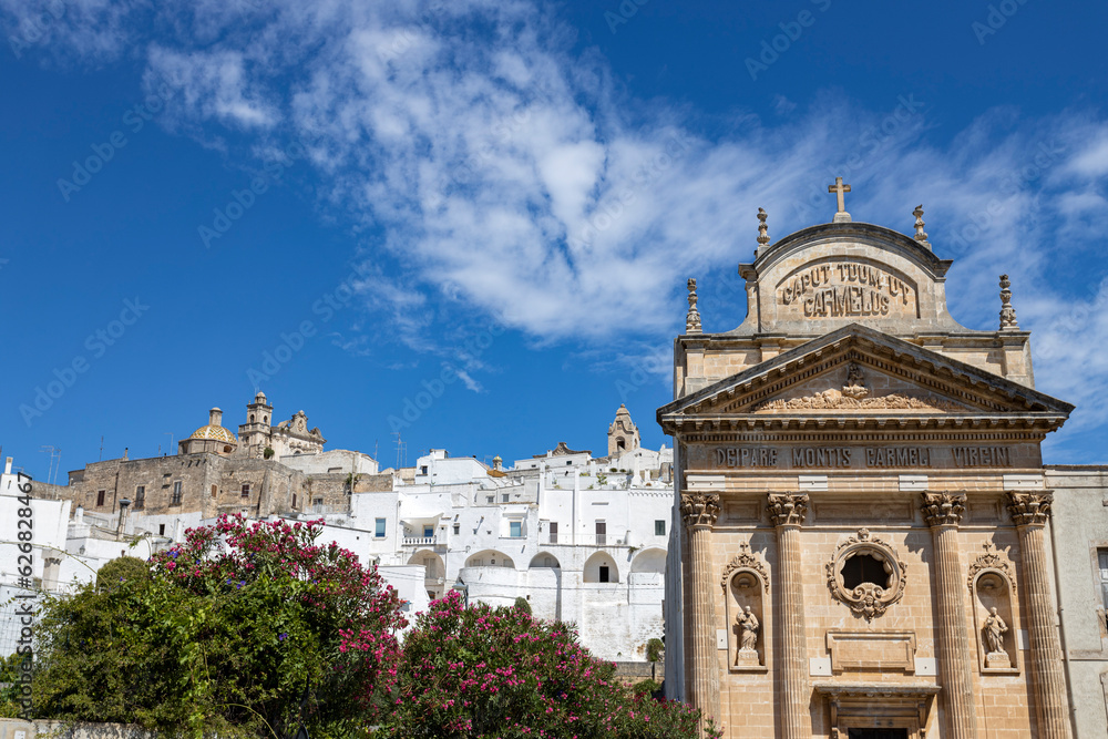OSTUNI, ITALY, JULY 12, 2022 - Landscape of Ostuni with the church Maria Santissima of Carmine in foreground, Province of Brindisi, Puglia, Italy
