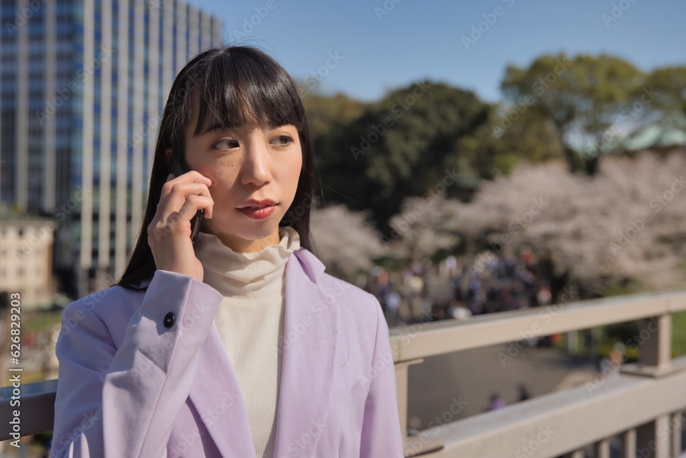 A portrait of Japanese woman calling a smartphone behind cherry blossom A portrait of Japanese woman calling a smartphone behind cherry blossom