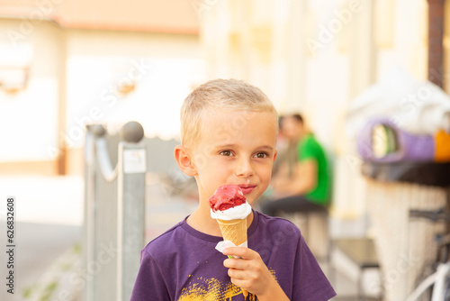 a boy stands on the street and eats red-white ice cream in a cone