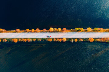 Aerial view of fall road and blue water lake sea ocean. Red car with a roof rack on a country road in Finland.