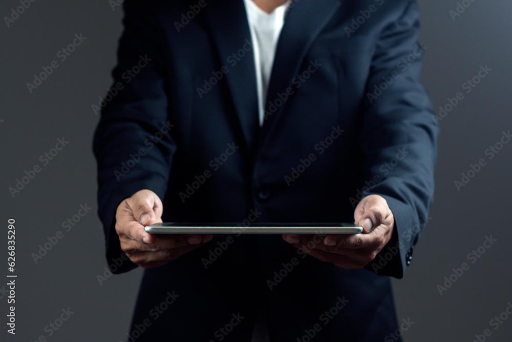 Businessman is holding digital tablet against dark background. Businessman is holding digital tablet against dark background.