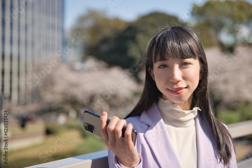 A portrait of Japanese woman with smartphone behind cherry blossom copyspace