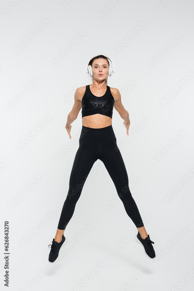brunette woman in black active wear and headphones jumping on white background, sport brunette woman in black active wear and headphones jumping on white background, sport
