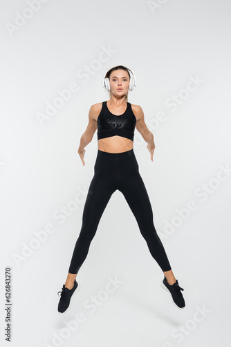 brunette woman in black active wear and headphones jumping on white background, sport © LIGHTFIELD STUDIOS
