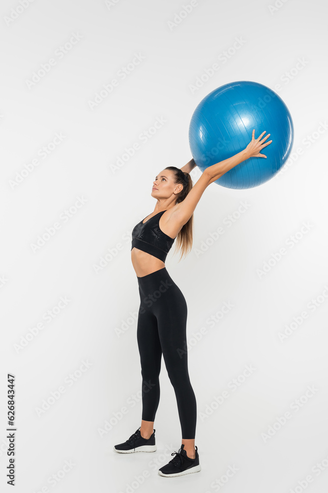 fit sportswoman in active wear and sneakers holding fitness ball and training on white background fit sportswoman in active wear and sneakers holding fitness ball and training on white background