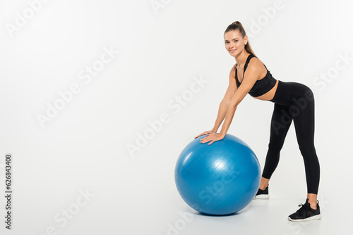 brunette sportswoman looking at camera while standing near fitness ball on white background
