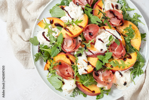 Healthy summer salad with peach, burrata, arugula and jamon