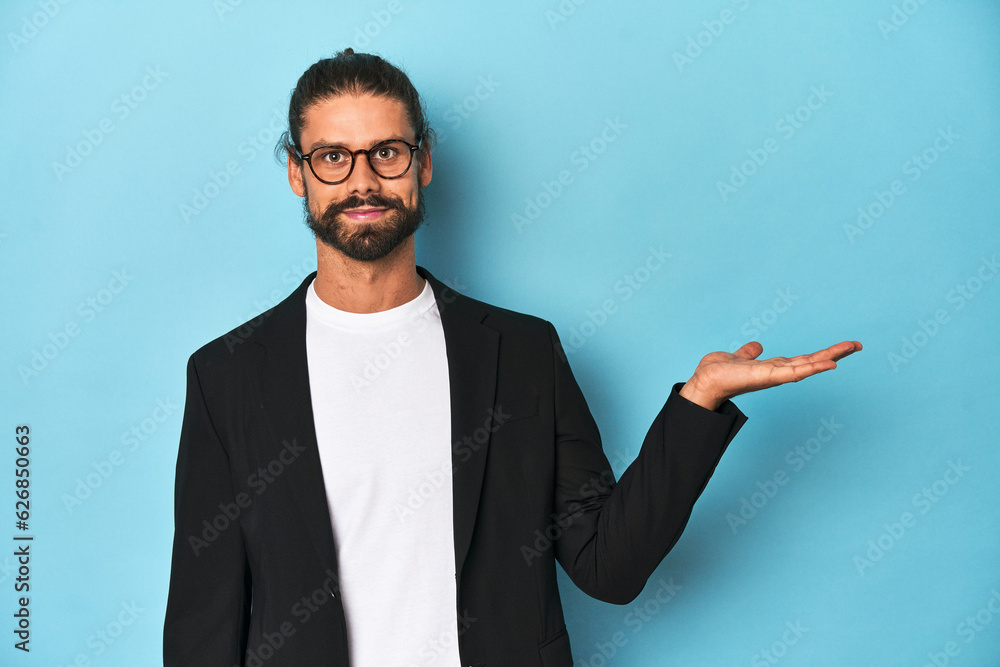 Businessman in suit with eyeglasses and beard showing a copy space on a palm and holding another hand on waist. Businessman in suit with eyeglasses and beard showing a copy space on a palm and holding another hand on waist.