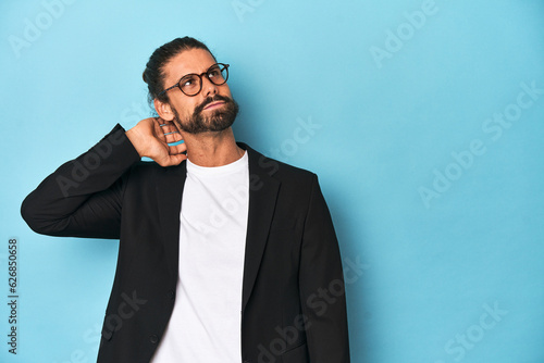 Businessman in suit with eyeglasses and beard touching back of head, thinking and making a choice. © Asier