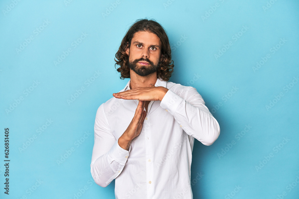Bearded man in a white shirt, blue backdrop showing a timeout gesture. Bearded man in a white shirt, blue backdrop showing a timeout gesture.