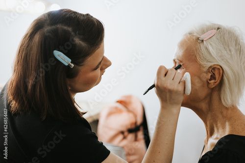 makeup for an age model, a girl does makeup in the studio for a beautiful adult elderly woman