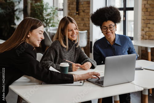 Three smiling women using laptop while working together in office