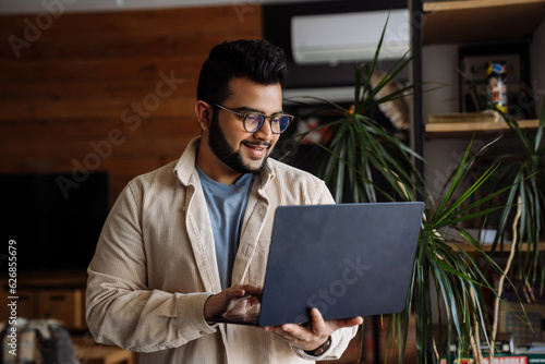 Smiling business man working on laptop while standing in office