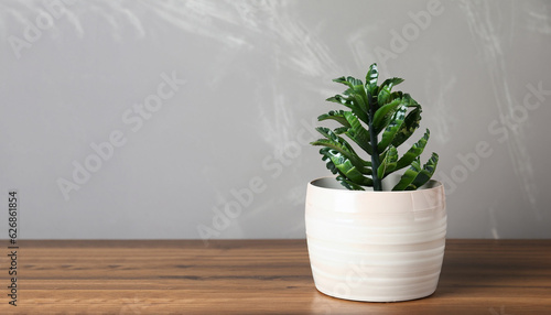 Beautiful artificial plant in flower pot on wooden table near grey wall  space for text