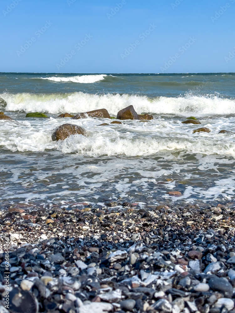 Waves in sea near coastline on empty pebble beach.