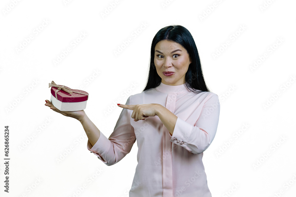 Asian brunette woman is pointing at heart-shaped gift box on her palm. Valentines day or anniversary. Isolated on white background. Asian brunette woman is pointing at heart-shaped gift box on her palm. Valentines day or anniversary. Isolated on white background.
