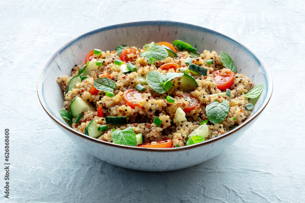 Quinoa tabbouleh salad in a bowl, a healthy dinner with tomatoes and mint, on a blue slate background