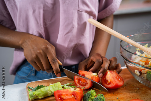 Young African woman in kitchen. Close up of woman making salad.