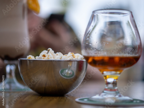 A milkshake next to a glass of whiskey and a bowl of popcorn.