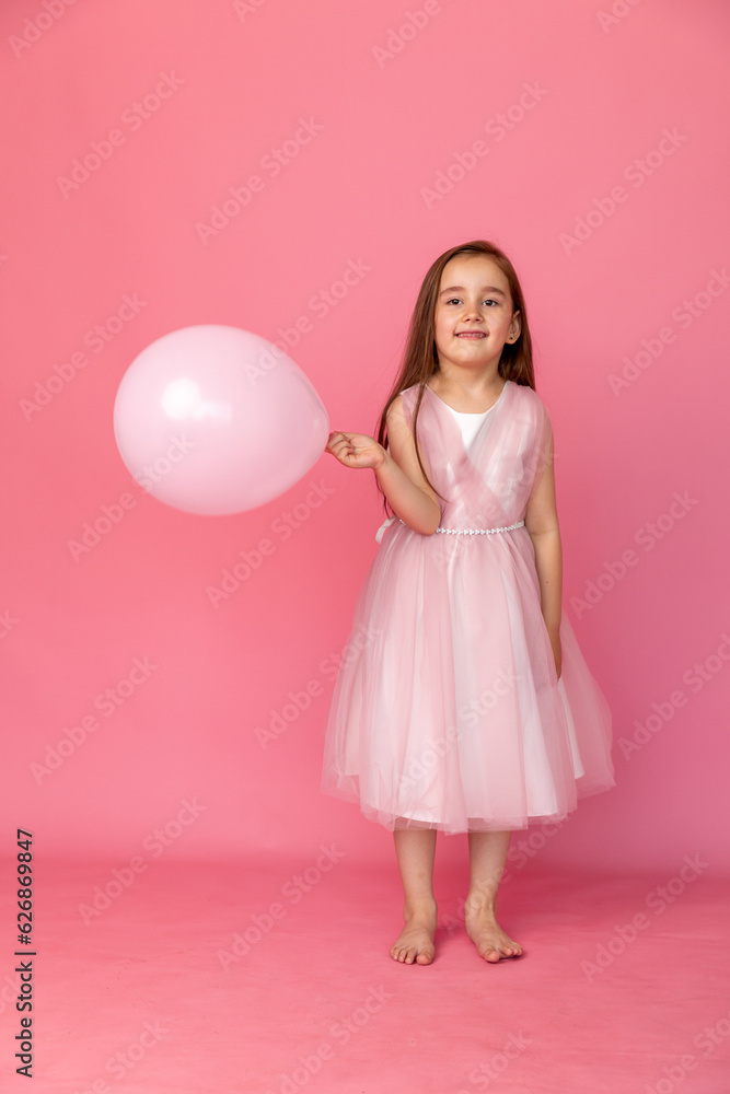 Cute smiling little girl in a pink princess dress posing with air balloon on pink background. Kids Birthday party celebration concept. Happy Birthday banner with copy space. Studio shot. Cute smiling little girl in a pink princess dress posing with air balloon on pink background. Kids Birthday party celebration concept. Happy Birthday banner with copy space. Studio shot.