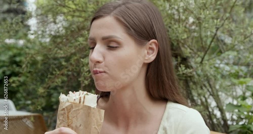 Beautiful young woman eating tasty fresh shawarma outdoors. Camera moving around girl
