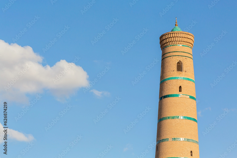 Minaret of the Juma Mosque, blue sky and fluffy clouds at background. Khiva, Uzbekistan.