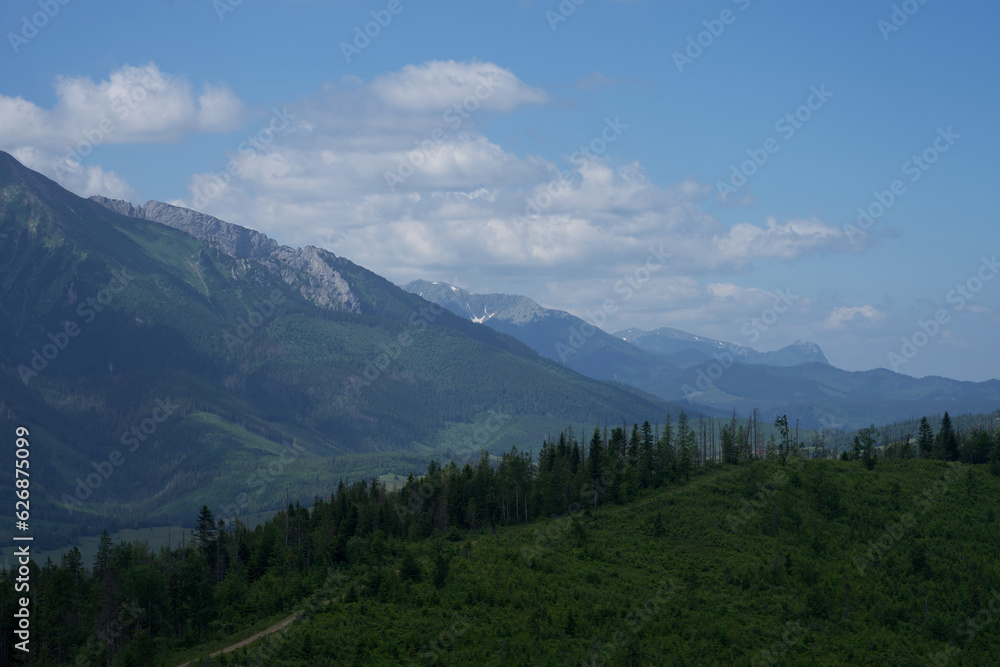 zdjęcie przedstawiające krajobraz górski wysokie szczyty i doliny nad którymi jest niebieskie niebo z kłębiącymi się chmurami. Lasy w dolinach gór, krajobraz górski natura i cisza i spokój