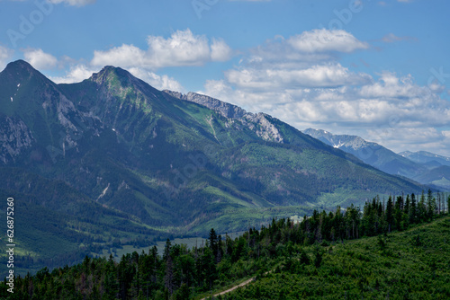 zdjęcie przedstawiające krajobraz górski wysokie szczyty i doliny nad którymi jest niebieskie niebo z kłębiącymi się chmurami. Lasy w dolinach gór, krajobraz górski natura i cisza i spokój © klumb