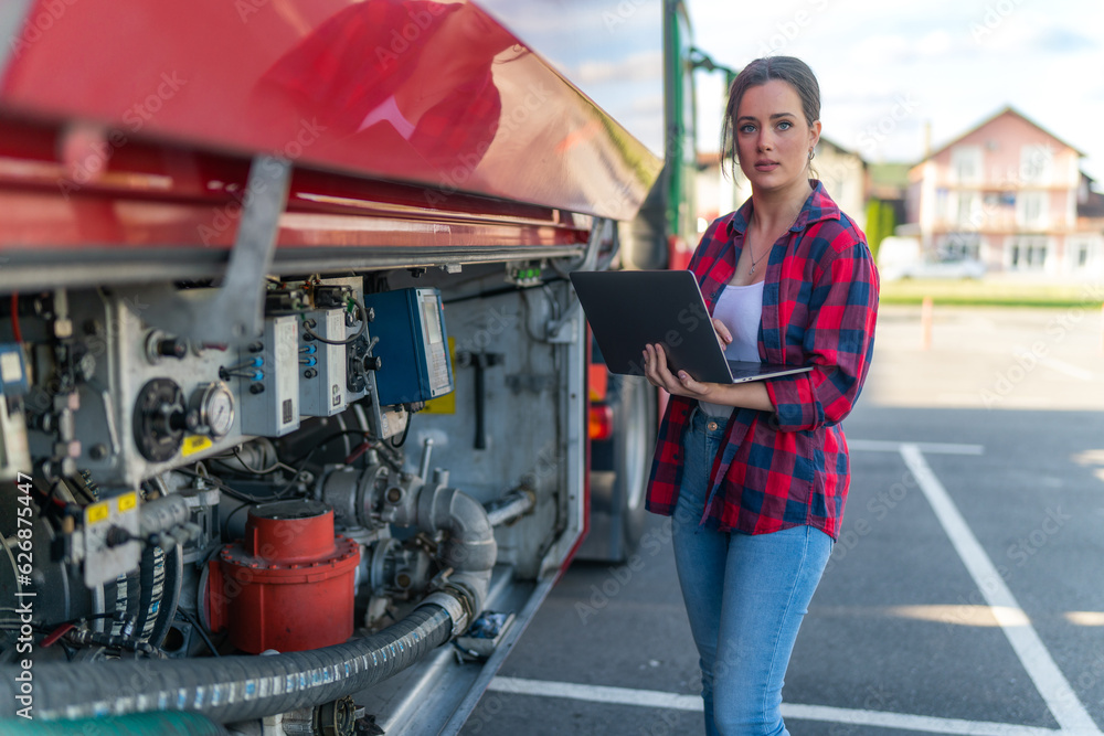 Truck driver holding a laptop and checking the fuel level in the tank, security checks for the safe transport of cargo Truck driver holding a laptop and checking the fuel level in the tank, security checks for the safe transport of cargo