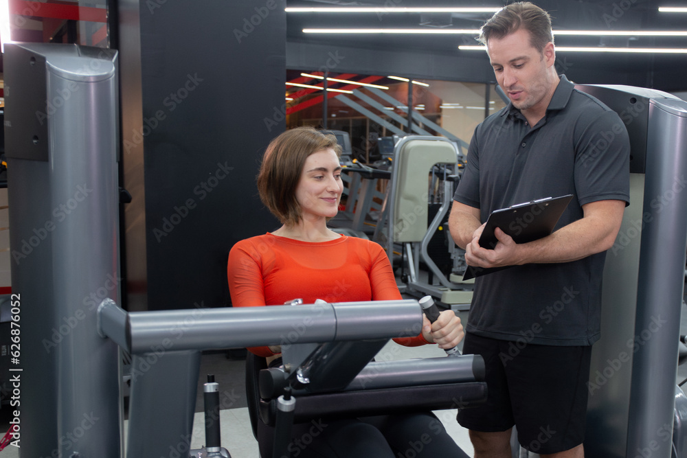 Fototapeta premium Coach man guidance workout with legs muscles stretch with equipment machine with woman in fitness gym club, strength and flexibility training, woman exercise with instructor or trainer, sport concept.