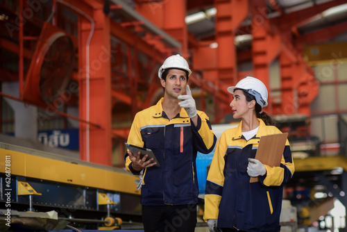 Latino male engineers industrial and female auditor wearing safety uniform workwear Walking to Audit and checking the safety of the work area and warehouse in an industrial factory.